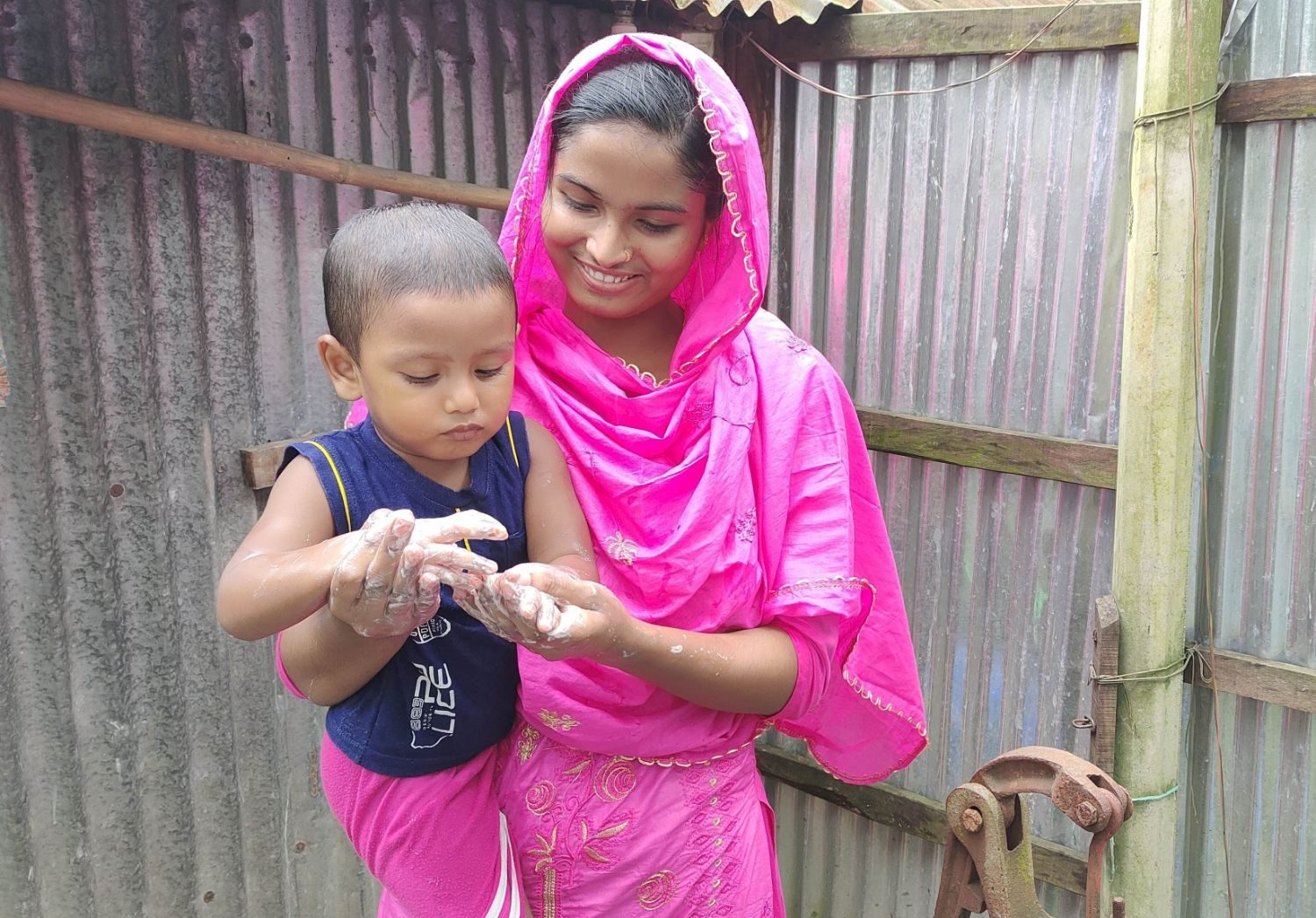A Health Leader teaches a young child to wash his hands with soap outside her home.