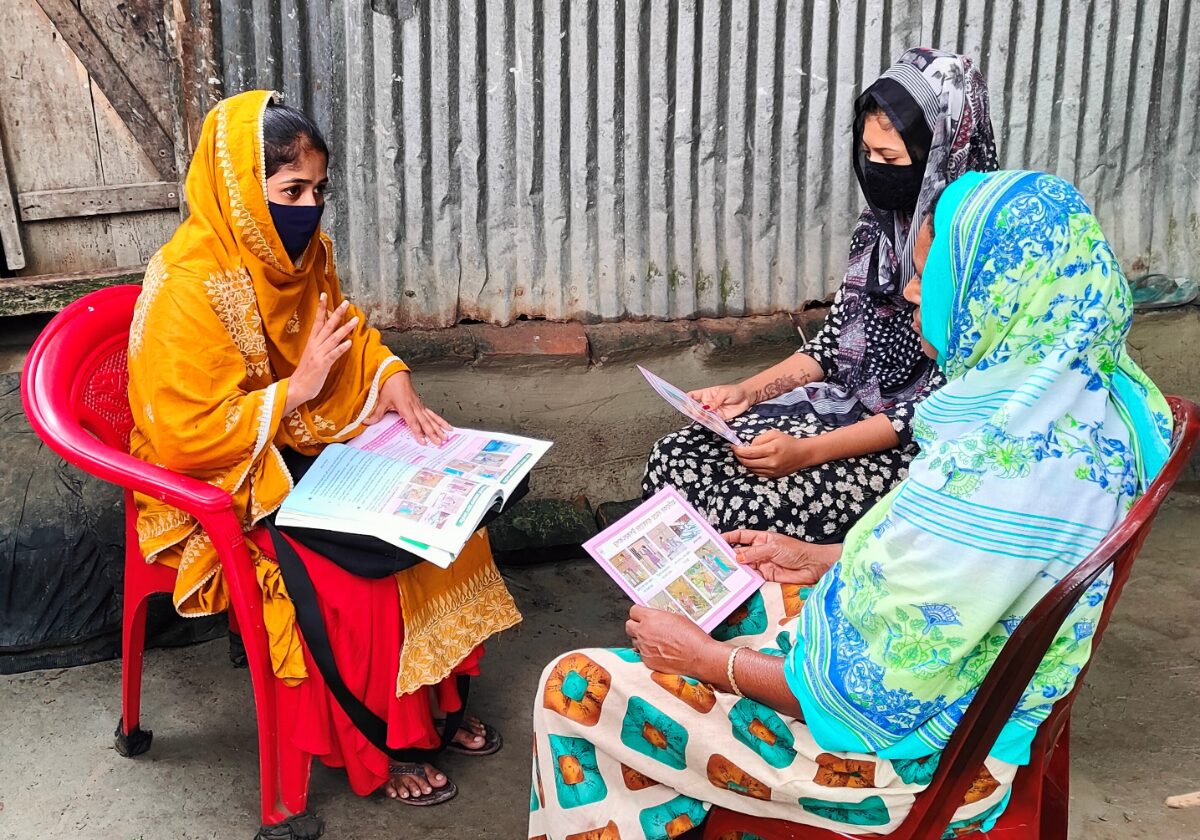 Two women sit outdoors working through illustrated health education booklets with a Health Leader.