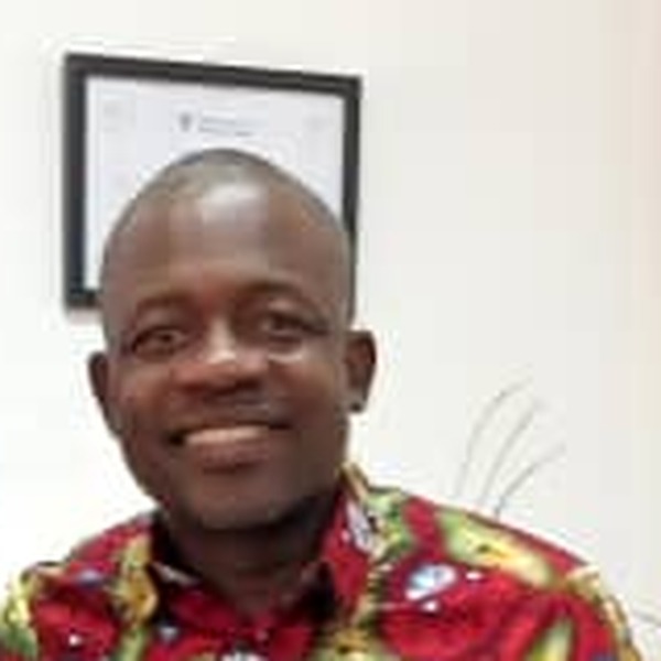 A man in a patterned shirt smiles at the camera in an office.